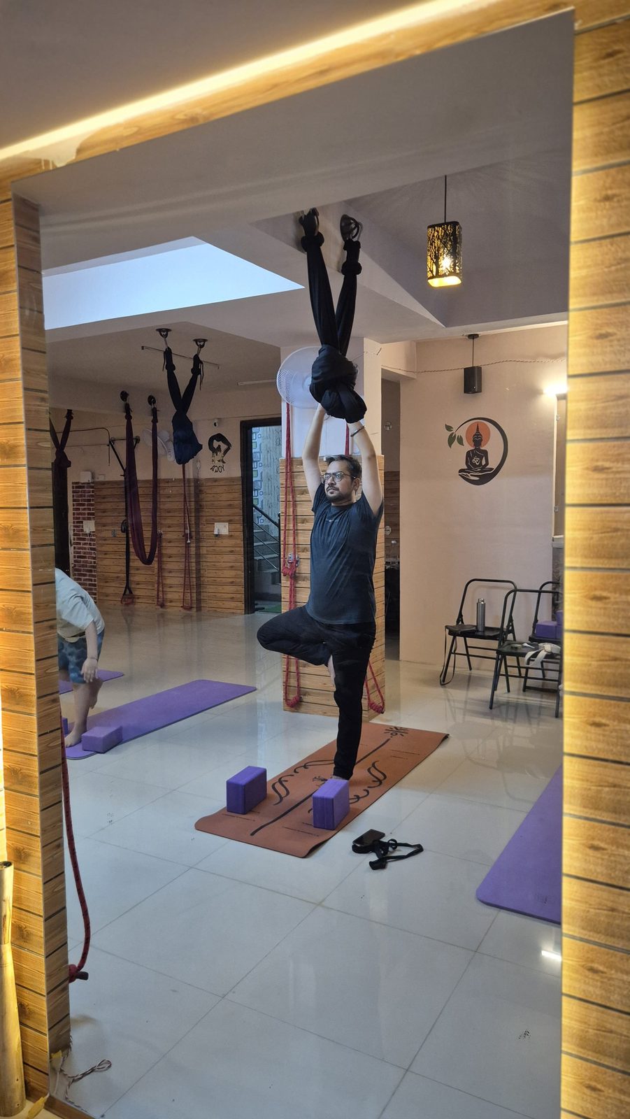 Student in Tree Pose supported by an aerial hammock under an archway