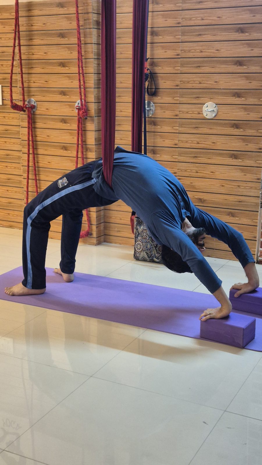 Student in a deep Wheel Pose against a wooden studio wall